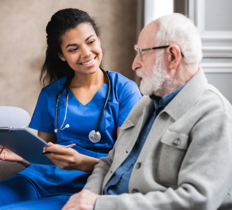 nurse holding a clipboard while talking to the elderly man