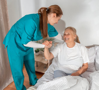 caregiver helping the elderly woman get up in bed