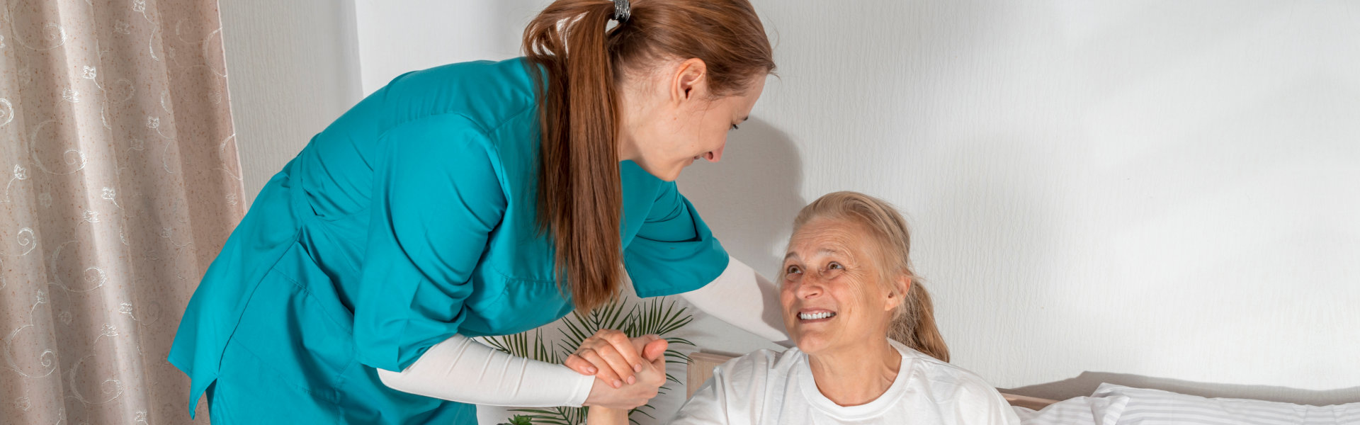 caregiver helping the elderly woman get up in bed