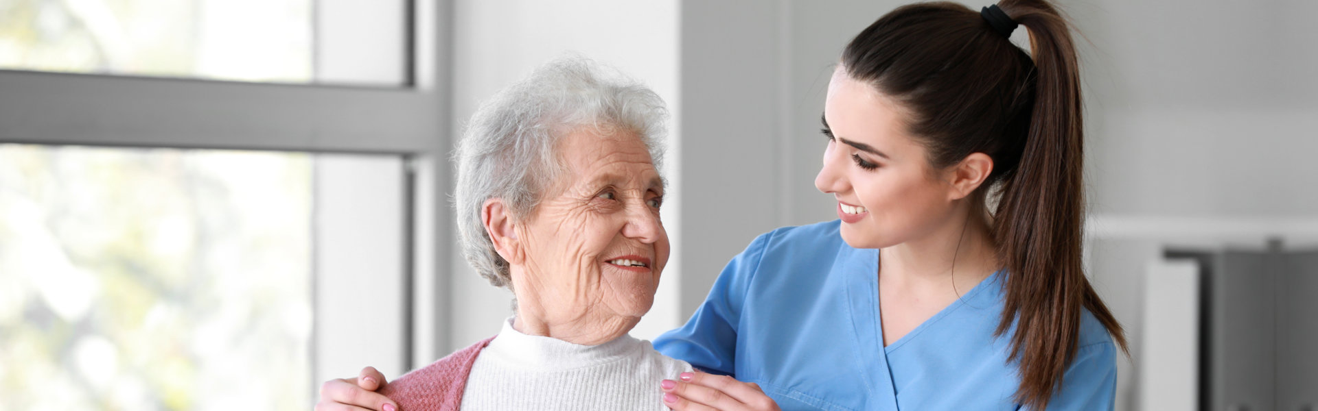 caregiver and elderly woman smiling while looking at each other